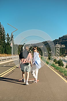 Positive man and woman walking in the mountains on the path holding hands on a sunny spring day. Vertical