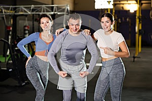 Positive man and young women in activewear posing during CrossFit workout in gym fitness center