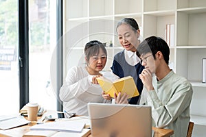 A positive mature Asian female professor teacher is explaining something in a book to her students