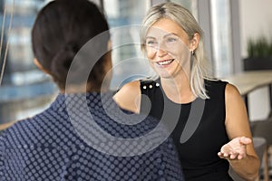 Positive mature businesswoman speaking to younger colleague