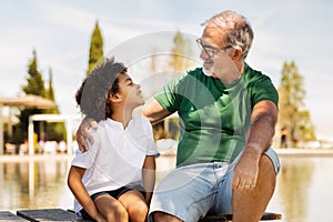 Positive mature caucasian grandfather and little mixed race boy enjoy free time, communicate, have fun