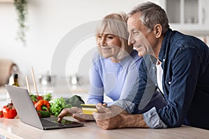 positive mature couple making online order, using notebok photo