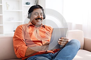 Positive mature indian man using digital tablet and headphones