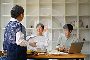 Positive mature lecturer talking to group of students during class. Education concept