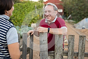 Positive mature man and woman standing near fence in garden
