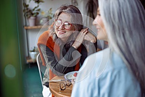 Positive mature woman with friend look through window sittin in cozy cafe