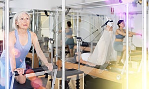 Mature woman practicing pilates stretching exercises on reformer at gym