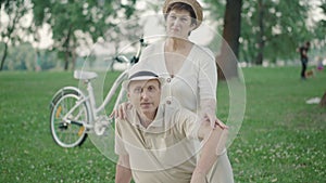 Positive mid-adult Caucasian couple posing on green summer lawn in park. Portrait of happy elegant man and woman looking