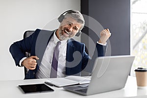 Positive Middle Aged Businessman Listening Music In Headphones And Playing Virtual Guitar