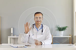 Positive middle aged man doctor in white medical uniformgreeting patient online
