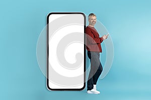 Positive middle aged man posing by big phone with mockup