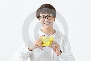 Positive middle-aged woman in glasses holds in hand a vintage yellow camera posing on a white background. Concept of