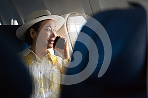 Positive middle aged woman tourist passenger talking on mobile phone and looking through airplane window.