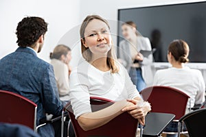 Positive middle-aged woman turning around and looking at camera during advanced training course in auditorium