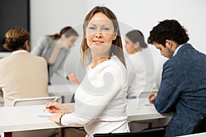 Positive middle-aged woman turning around and looking at camera during advanced training course in auditorium