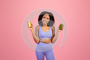 Positive millennial african american lady in sportswear hold jars of juice or smoothies, enjoy healthy drink