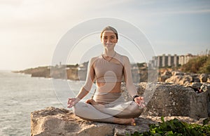 Positive millennial caucasian lady athlete in sportswear practices yoga in lotus position, meditates, enjoys rest