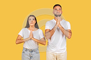 Positive millennial european family in white t-shirts hoping or wishing and make pray gesture, look up