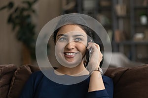 Positive millennial hindu woman relax on couch chat on phone