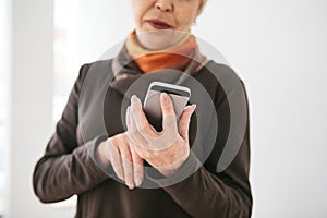 A positive modern elderly woman is holding a cell phone and is using it. The older generation and modern technology.