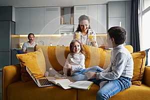 Positive mother bringing orange juice to children on sofa