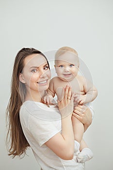 Positive mother with broad smile holds smiling baby on arms