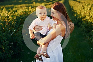 Positive mother with her son spending free time on the field at sunny day time of summer