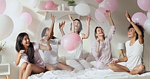 Positive multiethnic girls having fun with balloons celebrate pajama party