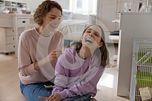 Positive mum and teen daughter playing with rat at home