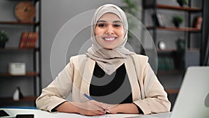 Positive Muslim woman manager accountant employee posing office desk workplace with positive emotion