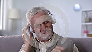 Positive old man in headphones listening to rock song, heavy metal from youth