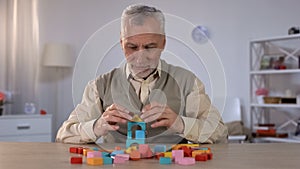 Positive old man playing with wooden cubes, cognitive training in Alzheimer photo