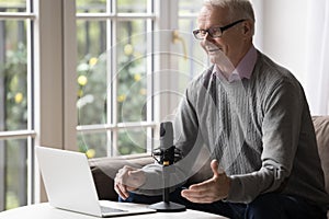 Positive old retired man speaking at microphone and laptop webcam