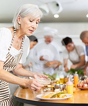 Positive old woman attendee of cooking course decorating meal made of salmon fish