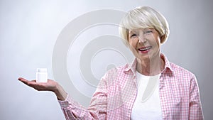 Positive old woman proposing pills jar, vitamins for health support, treatment