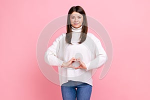 Positive optimistic brunette female showing heart shape in front of belly as symbol of women health.