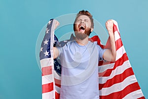 Positive overjoed bearded man holds huge american flag, rejoicing while celebrating national holiday