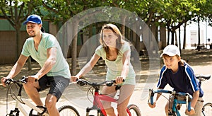 Positive parents with kid riding bicycles in park