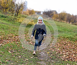 A photo of a laughing carefree little girl running on a path in an autumn park