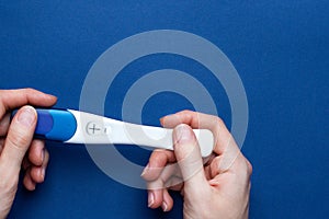 Positive pregnancy test in female hands on blue background