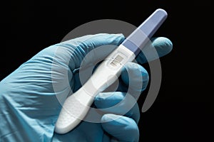 Positive pregnancy test with two strips in the doctor`s hand in a blue medical glove against a black background