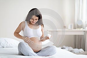 Positive pregnant woman applying belly butter on her big tummy
