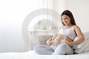 Positive pregnant woman holding headphones on her big belly, panorama