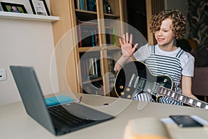 Positive preteen girl greeting and learning to play the guitar in virtual meeting together with teacher in video call.