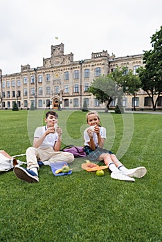 Positive preteen schoolkids holding sandwiches near