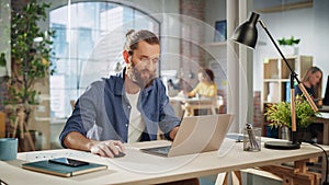 Positive Project Manager Sitting at a Desk, Working on a Laptop Computer in an Office. Creative