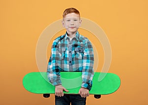 Positive red-haired boy with skateboard deck on yellow