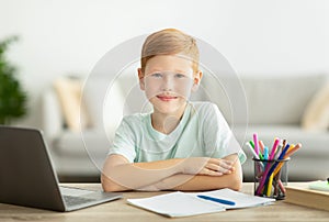 Positive redhead boy schooler doing homework at home