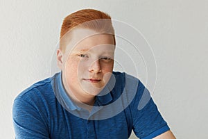 A positive redhead guy with freckles and brown eyes dressed in blue shirt looking mysteriously into camera isolated over white bac