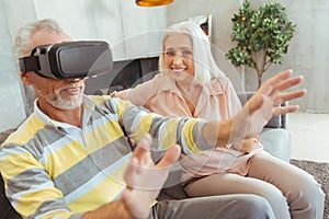 Positive retired man wearing VR glasses at home